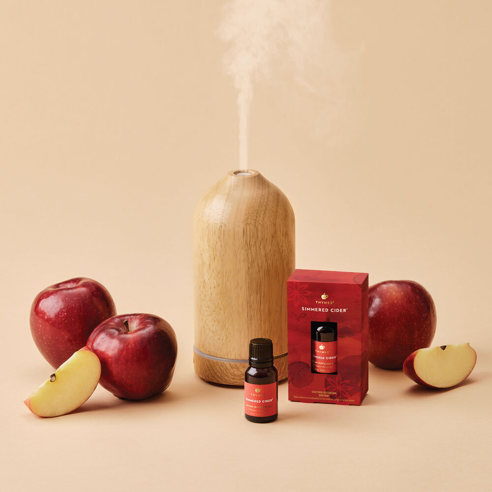 Thymes Simmered Cider Diffuser Oil Beside Electric Diffuser and Apples image number 1